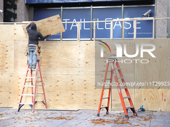 Workers cover storefront entrances with plywood near the White House in Washington, D.C. on November 1, 2024 in preparation for possible civ...