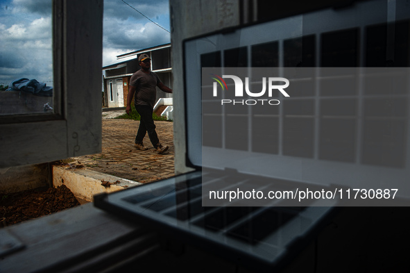 A worker, Wahyu, 31, repairs a water installation with the foreground of an emergency solar power plant at a house in the new subsidized set...