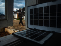 A worker, Wahyu, 31, repairs a water installation with the foreground of an emergency solar power plant at a house in the new subsidized set...