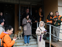 People stand at an entrance to a 16-storey residential building in the Sviatoshynskyi district damaged by falling Russian drone debris in Ky...