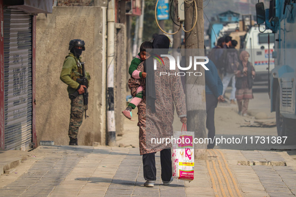 A woman holds her child as an Indian security personnel stands guard near the site of a gunbattle between suspected militants and security f...