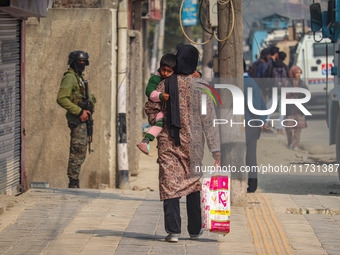 A woman holds her child as an Indian security personnel stands guard near the site of a gunbattle between suspected militants and security f...