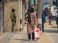 A woman holds her child as an Indian security personnel stands guard near the site of a gunbattle between suspected militants and security f...