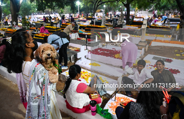 A family with a pet dog prays next to the grave of departed ones to commemorate All Souls Day at a cemetery in Hyderabad, on November 2, 202...