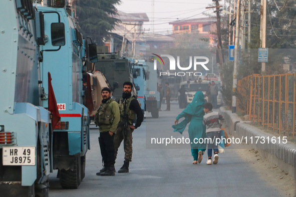 People walk as Indian paramilitary troopers remain alert near the encounter site in Srinagar, Indian Administered Kashmir, on November 2, 20...