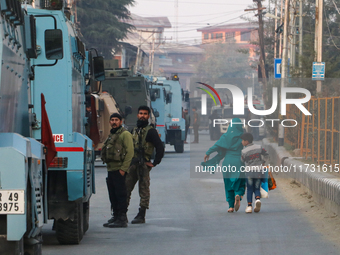 People walk as Indian paramilitary troopers remain alert near the encounter site in Srinagar, Indian Administered Kashmir, on November 2, 20...