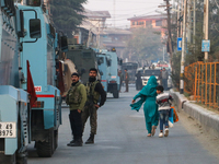 People walk as Indian paramilitary troopers remain alert near the encounter site in Srinagar, Indian Administered Kashmir, on November 2, 20...