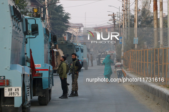 People walk as Indian paramilitary troopers remain alert near the encounter site in Srinagar, Indian Administered Kashmir, on November 2, 20...