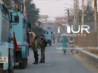 People walk as Indian paramilitary troopers remain alert near the encounter site in Srinagar, Indian Administered Kashmir, on November 2, 20...