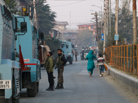 People walk as Indian paramilitary troopers remain alert near the encounter site in Srinagar, Indian Administered Kashmir, on November 2, 20...