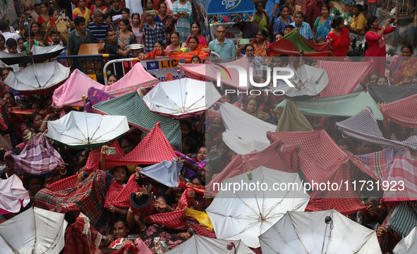 Hindu devotees hold up clothes and umbrellas to receive rice as offerings distributed by the temple authority on the occasion of the Annakut...