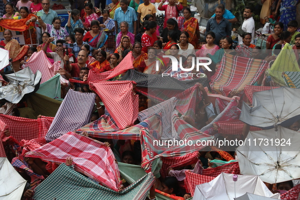 Hindu devotees hold up clothes and umbrellas to receive rice as offerings distributed by the temple authority on the occasion of the Annakut...