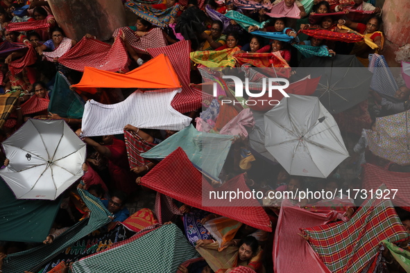 Hindu devotees hold up clothes and umbrellas to receive rice as offerings distributed by the temple authority on the occasion of the Annakut...