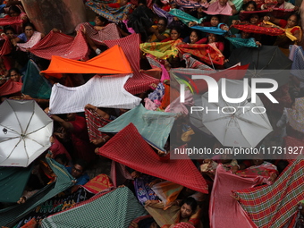 Hindu devotees hold up clothes and umbrellas to receive rice as offerings distributed by the temple authority on the occasion of the Annakut...