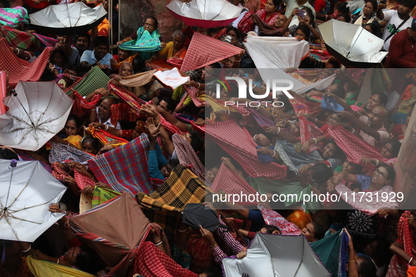 Hindu devotees hold up clothes and umbrellas to receive rice as offerings distributed by the temple authority on the occasion of the Annakut...