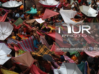 Hindu devotees hold up clothes and umbrellas to receive rice as offerings distributed by the temple authority on the occasion of the Annakut...