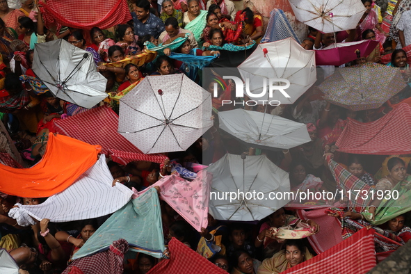 Hindu devotees hold up clothes and umbrellas to receive rice as offerings distributed by the temple authority on the occasion of the Annakut...