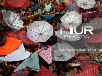 Hindu devotees hold up clothes and umbrellas to receive rice as offerings distributed by the temple authority on the occasion of the Annakut...