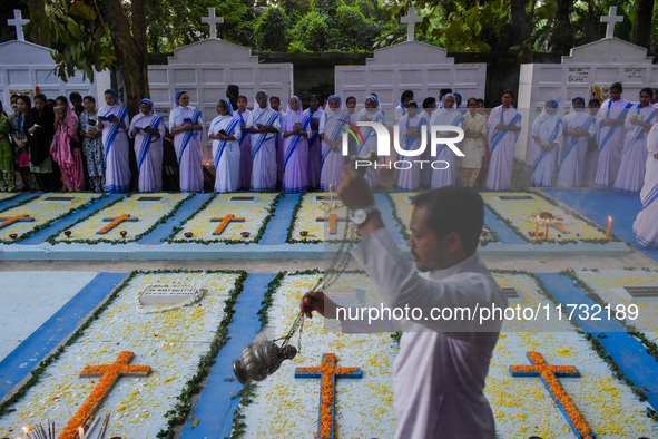 Sisters of Missionaries of Charity pray as a father spreads incense in front of graves during All Souls' Day observance at a cemetery 80 kil...