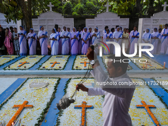 Sisters of Missionaries of Charity pray as a father spreads incense in front of graves during All Souls' Day observance at a cemetery 80 kil...