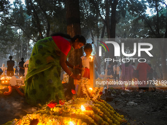 A mother and child light candles over her relative's grave during All Souls Day observance at a cemetery 80 kilometers outside of Kolkata, I...