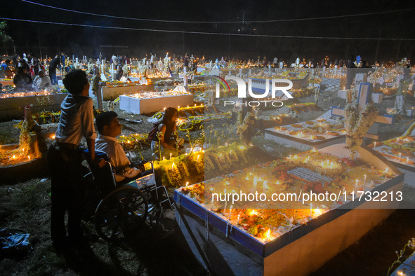 A man in a wheelchair is in front of the grave of his relative during All Souls' Day observance at a cemetery 80 kilometers outside Kolkata,...