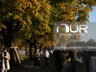 People walk among trees with autumn yellow leaves in Krakow, Poland, on October 19, 2024. (