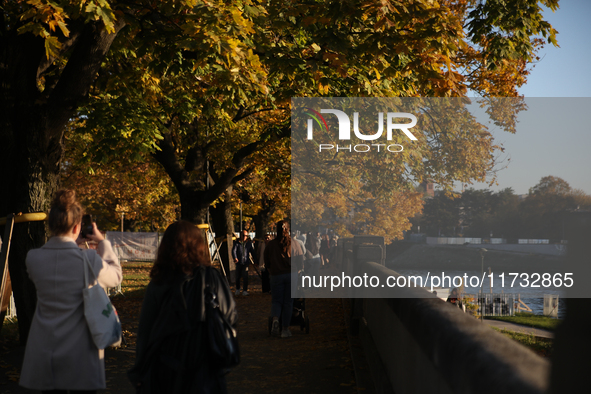 People walk among trees with autumn yellow leaves in Krakow, Poland, on October 19, 2024. 