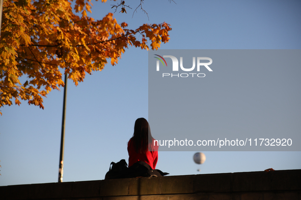 A woman sits among trees with autumn yellow leaves in Krakow, Poland, on October 19, 2024. 