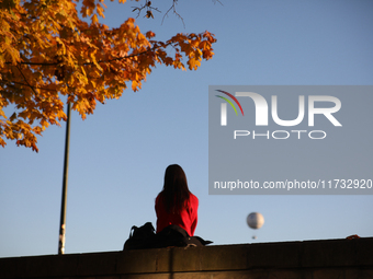 A woman sits among trees with autumn yellow leaves in Krakow, Poland, on October 19, 2024. (