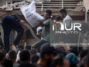 Palestinians scramble to receive sacks of flour at a United Nations Relief and Works Agency (UNRWA) aid distribution center amid the Israel-...