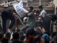 Palestinians scramble to receive sacks of flour at a United Nations Relief and Works Agency (UNRWA) aid distribution center amid the Israel-...