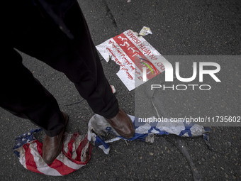 An Iranian protester stands on burnt U.S. and Israeli flags while participating in an anti-U.S. and anti-Israel rally marking the anniversar...