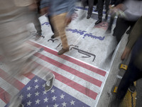 Iranian protesters walk on the U.S. flag and a banner featuring a portrait of the former U.S. President, Donald Trump, while participating i...