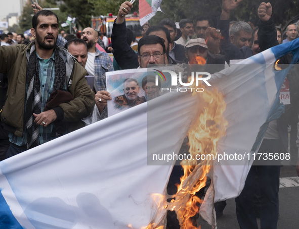 An Iranian man holds a poster featuring portraits of Lebanon's Hezbollah late leader, Hassan Nasrallah, and an IRGC's Quds Force commander,...