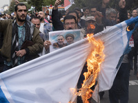 An Iranian man holds a poster featuring portraits of Lebanon's Hezbollah late leader, Hassan Nasrallah, and an IRGC's Quds Force commander,...