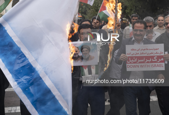 An Iranian man holds a poster featuring portraits of Lebanon's Hezbollah late leader, Hassan Nasrallah, and an IRGC's Quds Force commander,...