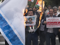 An Iranian man holds a poster featuring portraits of Lebanon's Hezbollah late leader, Hassan Nasrallah, and an IRGC's Quds Force commander,...