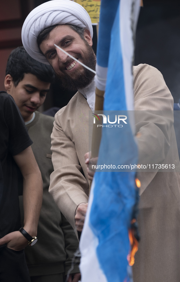 An Iranian cleric smiles while burning an Israeli flag out of the former U.S. embassy during an anti-U.S. and anti-Israel rally marking the...