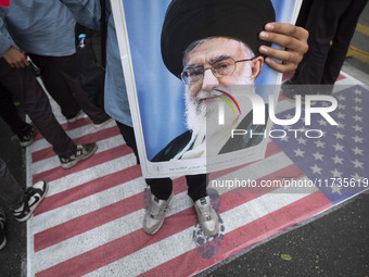 An Iranian student holds a portrait of Iran's Supreme Leader, Ayatollah Ali Khamenei, while standing on the U.S. flag during an anti-U.S. an...