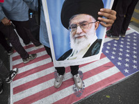 An Iranian student holds a portrait of Iran's Supreme Leader, Ayatollah Ali Khamenei, while standing on the U.S. flag during an anti-U.S. an...