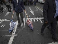 An Iranian man carries the U.S. and Israel flags while participating in an anti-U.S. and anti-Israel rally marking the anniversary of the U....