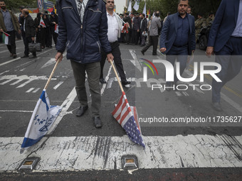 An Iranian man carries the U.S. and Israel flags while participating in an anti-U.S. and anti-Israel rally marking the anniversary of the U....