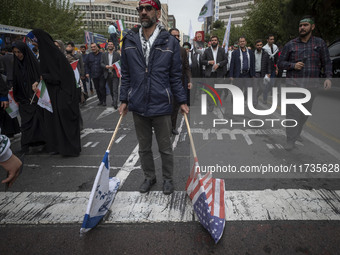 An Iranian man carries the U.S. and Israel flags while participating in an anti-U.S. and anti-Israel rally marking the anniversary of the U....