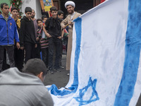 An Iranian cleric prepares an Israeli flag to set on fire outside the former U.S. embassy during an anti-U.S. and anti-Israel rally marking...