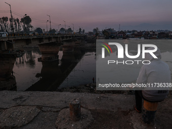 A man sits on a concrete block and watches Kashmiri boys catch fish on a cold evening in River Jhelum in Sopore, Jammu and Kashmir, India, o...