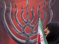 A veiled Iranian woman carries an Iranian flag and walks past an anti-Israeli banner while participating in an anti-U.S. and anti-Israel ral...