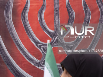 A veiled Iranian woman carries an Iranian flag and walks past an anti-Israeli banner while participating in an anti-U.S. and anti-Israel ral...