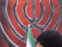 A veiled Iranian woman carries an Iranian flag and walks past an anti-Israeli banner while participating in an anti-U.S. and anti-Israel ral...