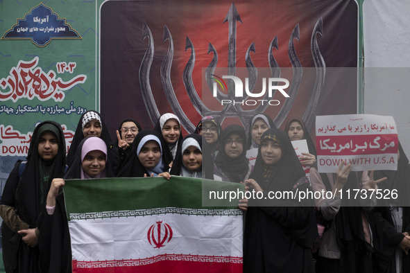 A group of veiled Iranian schoolgirls pose for a photograph while holding an Iranian flag in front of an anti-Israeli banner during an anti-...